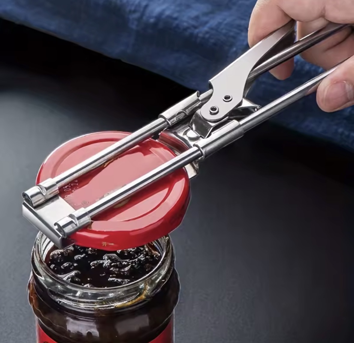 A hand-operated clamping opener gripping a jar lid
